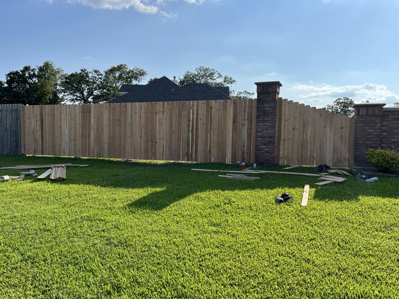 Wood privacy fence with brick columns around a large green backyard